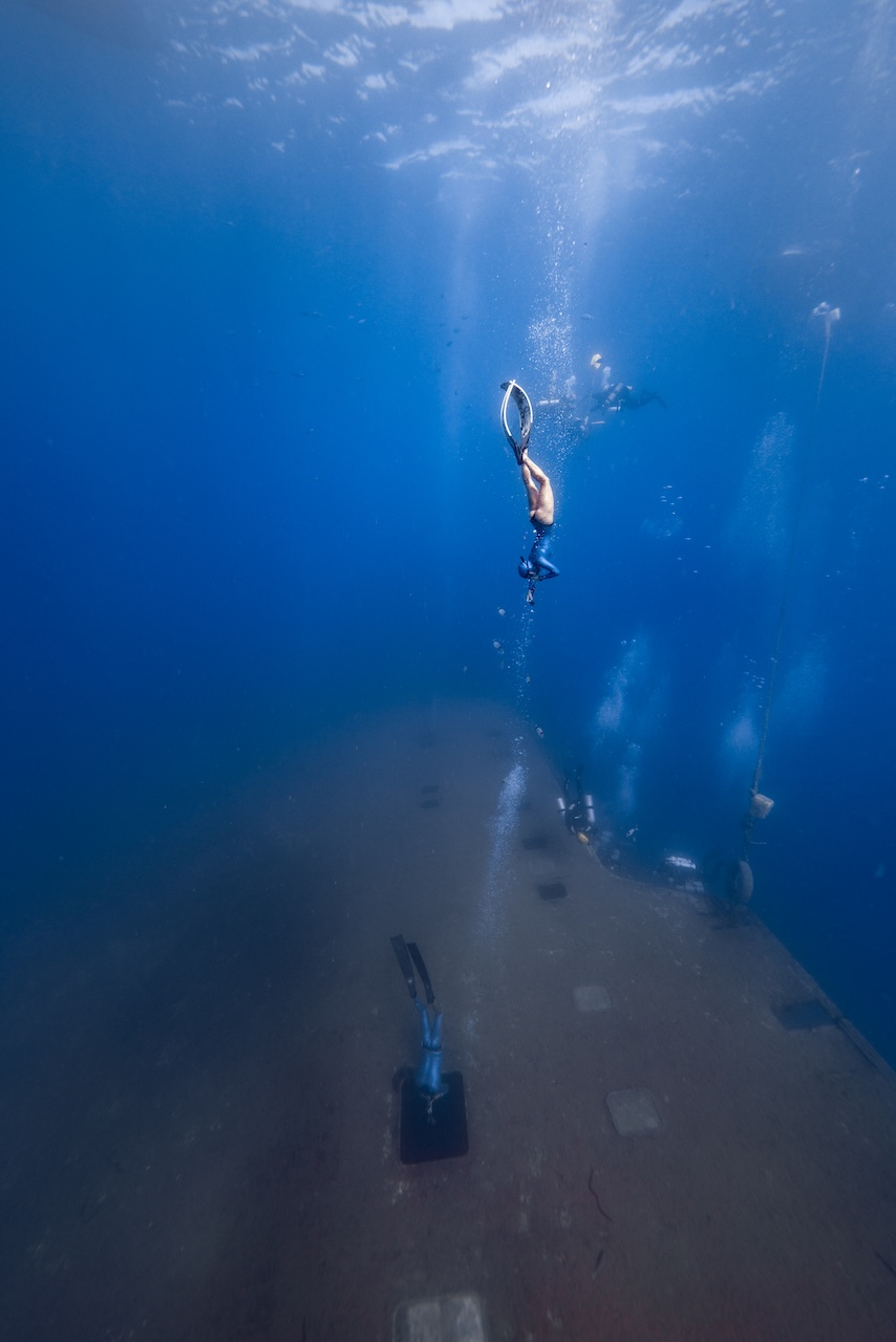 Freediver descending toward a Mediterranean shipwreck deck