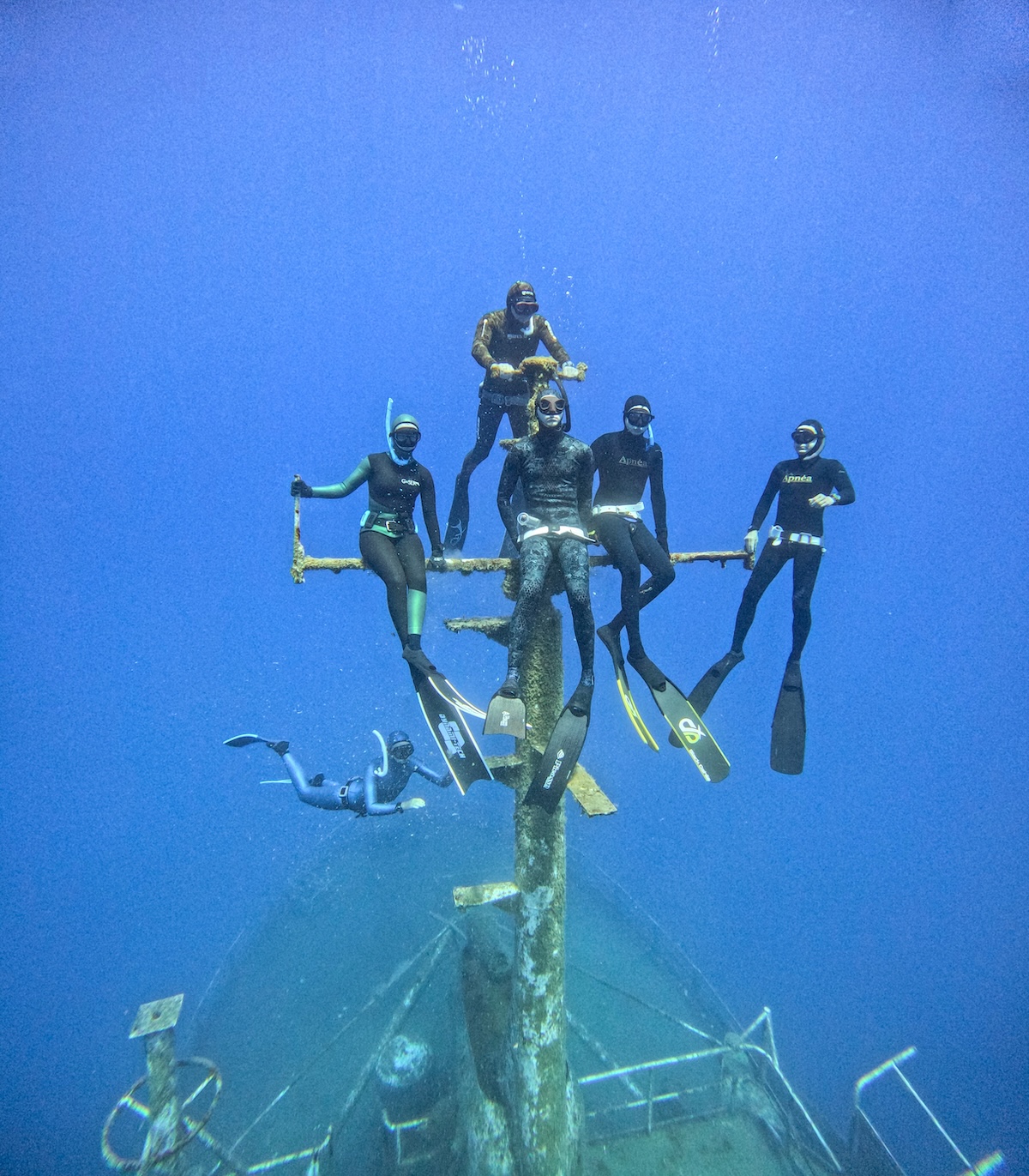 Freedivers gliding above a Mediterranean wreck mast at depth